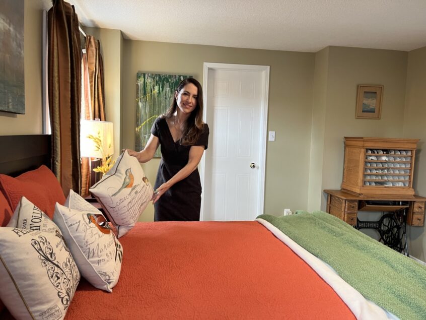 Realtor Helen staging a bedroom with orange and green bedding by adjusting pillows on the bed.